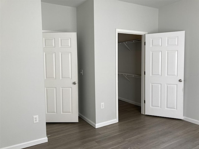 unfurnished bedroom with a closet, baseboards, a walk in closet, and wood finished floors