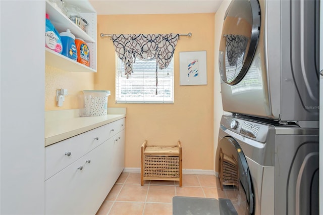 washroom featuring light tile patterned floors, stacked washer / drying machine, cabinet space, and baseboards