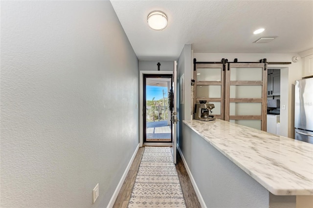 interior space with visible vents, baseboards, light stone countertops, freestanding refrigerator, and wood finished floors