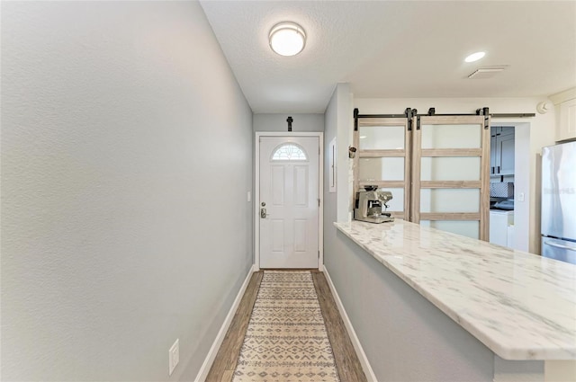 doorway featuring visible vents, baseboards, a barn door, light wood-style floors, and a textured ceiling