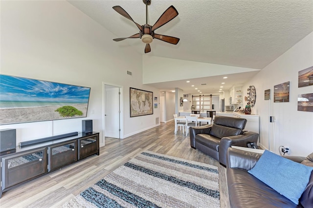 living room with light wood-type flooring, visible vents, a textured ceiling, baseboards, and ceiling fan