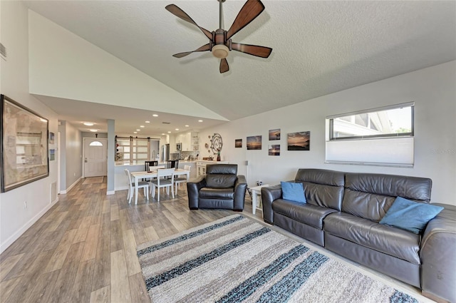 living area featuring high vaulted ceiling, light wood-style flooring, a ceiling fan, a textured ceiling, and baseboards