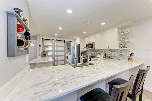 kitchen featuring visible vents, open shelves, stainless steel appliances, a barn door, and backsplash