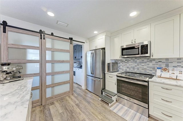 kitchen featuring visible vents, a barn door, light wood-style flooring, stainless steel appliances, and white cabinetry