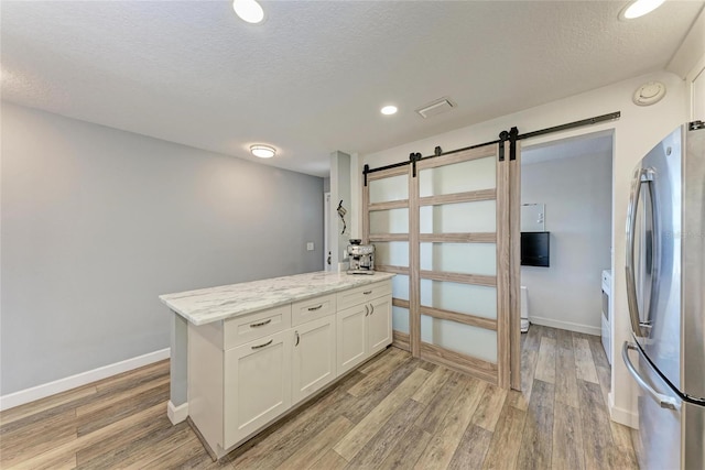 kitchen with light wood-style floors, visible vents, freestanding refrigerator, and a barn door