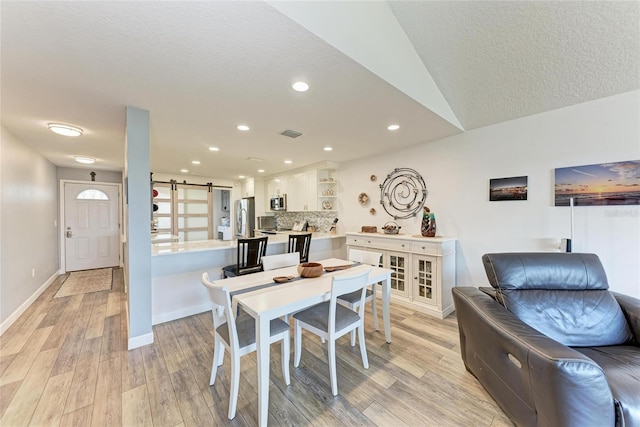 dining space with visible vents, baseboards, light wood-type flooring, a barn door, and recessed lighting