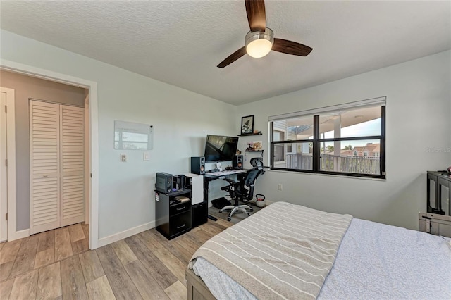 bedroom featuring light wood-style flooring, a textured ceiling, baseboards, and ceiling fan