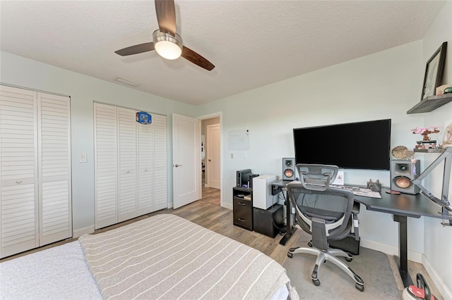 bedroom featuring two closets, light wood-style flooring, a ceiling fan, and a textured ceiling