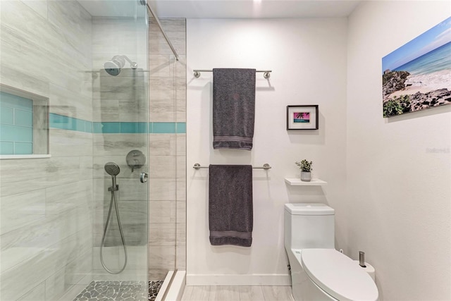 bathroom with a stall shower, toilet, and baseboards