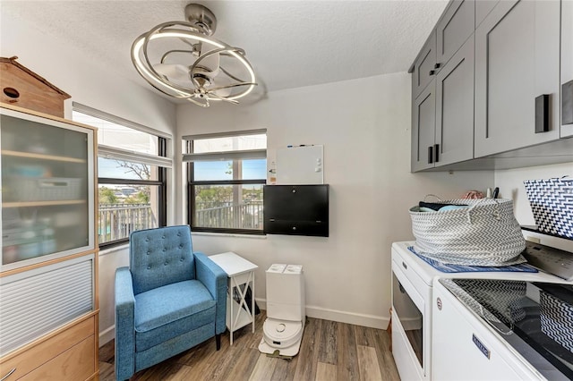 living area with washer and dryer, a textured ceiling, baseboards, and wood finished floors