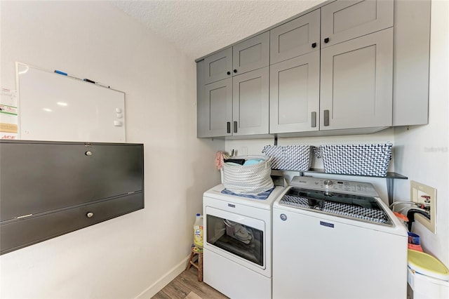 laundry room featuring a textured ceiling, washing machine and dryer, cabinet space, light wood finished floors, and baseboards