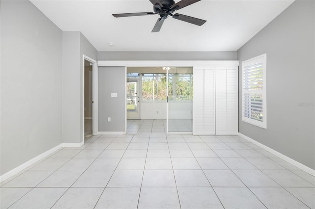 empty room featuring light tile patterned floors, baseboards, a healthy amount of sunlight, and a ceiling fan