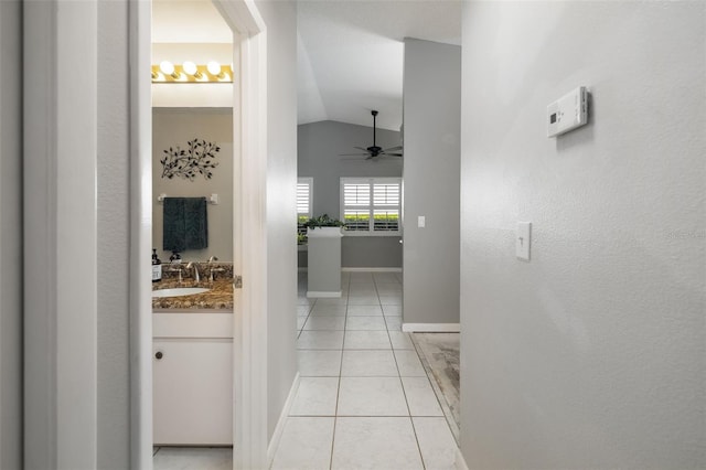 hall with light tile patterned floors, baseboards, lofted ceiling, and a sink