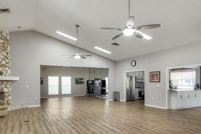 unfurnished living room featuring a stone fireplace, light wood-style flooring, visible vents, and high vaulted ceiling