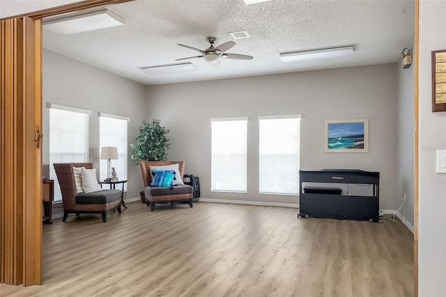 living area with visible vents, baseboards, ceiling fan, light wood-style floors, and a textured ceiling