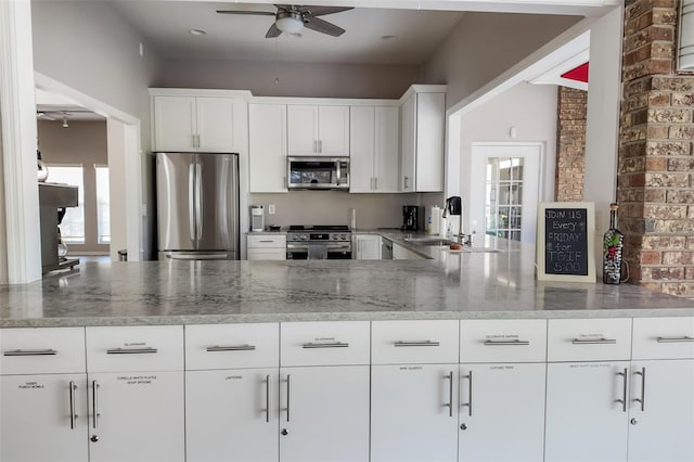 kitchen with a sink, stainless steel appliances, a peninsula, light stone countertops, and ceiling fan