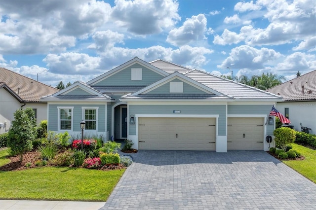 view of front of house featuring decorative driveway, a tile roof, an attached garage, and a front yard