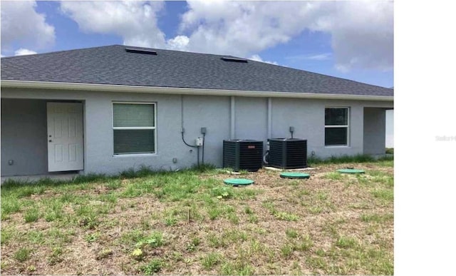 back of property with stucco siding, cooling unit, and a shingled roof