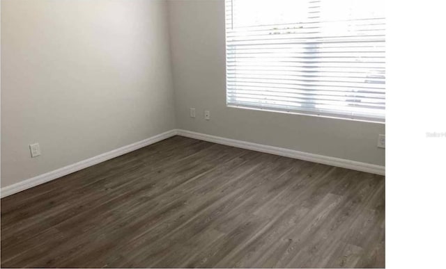 empty room featuring baseboards and dark wood-type flooring