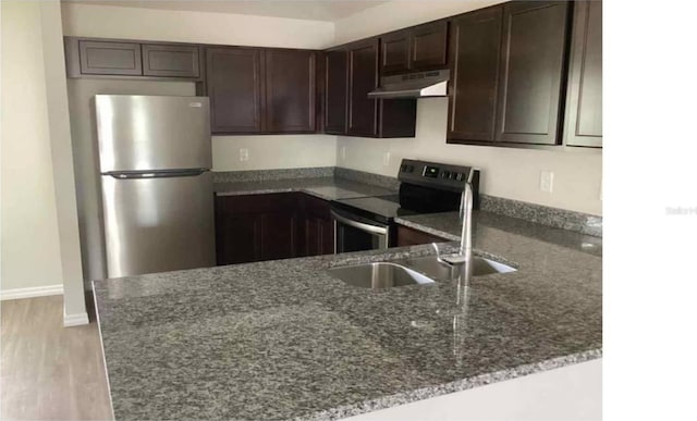 kitchen with under cabinet range hood, dark brown cabinetry, dark stone countertops, appliances with stainless steel finishes, and a sink