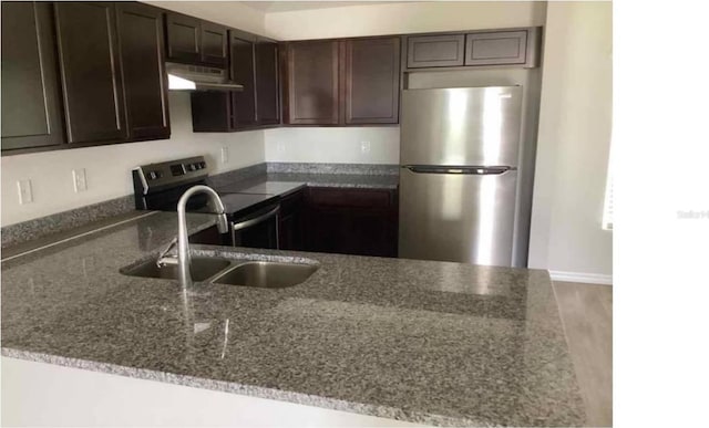 kitchen featuring dark stone counters, a sink, stainless steel appliances, dark brown cabinetry, and exhaust hood