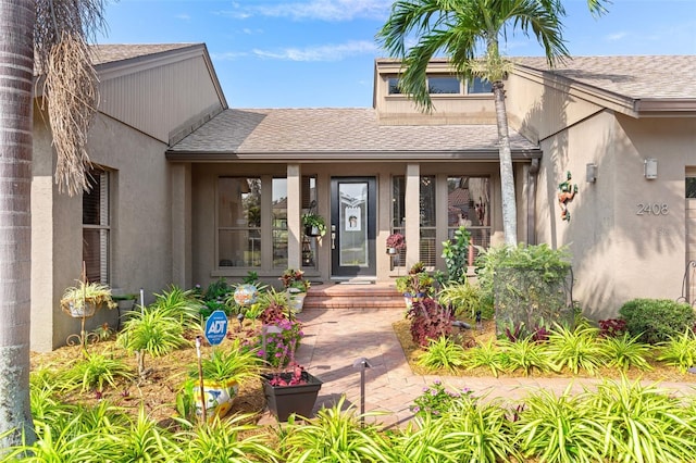 entrance to property featuring roof with shingles and stucco siding