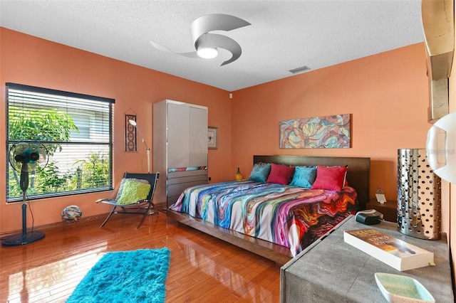 bedroom featuring visible vents, a textured ceiling, ceiling fan, and wood finished floors