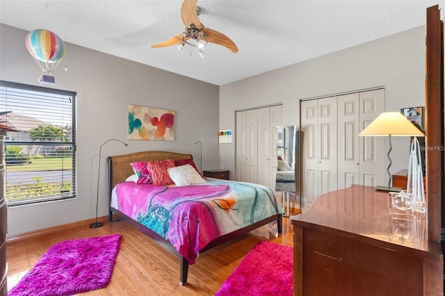 bedroom with ceiling fan, baseboards, multiple closets, and wood finished floors