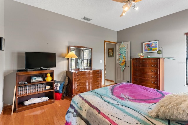 bedroom with a ceiling fan, wood finished floors, and visible vents