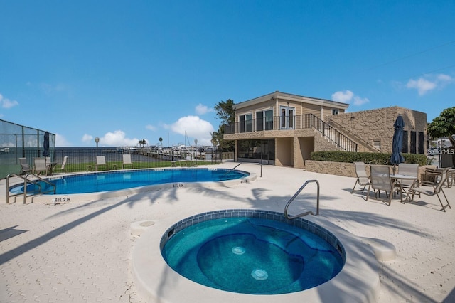 community pool with a patio area, a community hot tub, stairs, and fence