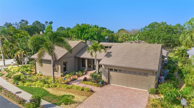 view of front facade featuring a garage, stucco siding, decorative driveway, and roof with shingles