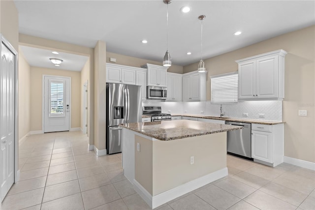 kitchen with light stone countertops, a sink, stainless steel appliances, tasteful backsplash, and a center island