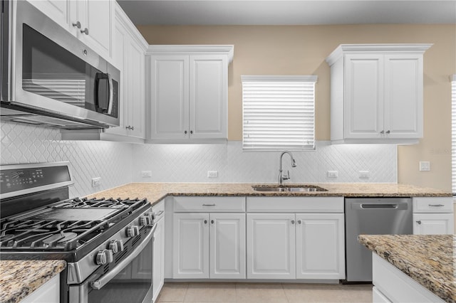 kitchen featuring light stone counters, white cabinetry, stainless steel appliances, and a sink