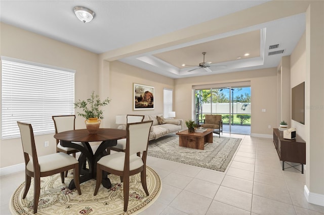 dining room with light tile patterned floors, visible vents, baseboards, a tray ceiling, and ceiling fan