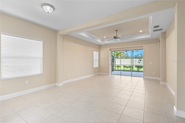 empty room with visible vents, a raised ceiling, a ceiling fan, light tile patterned floors, and baseboards