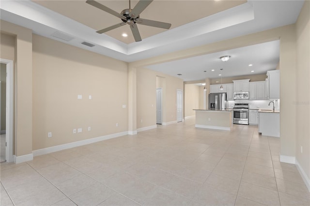 unfurnished living room with visible vents, baseboards, ceiling fan, a tray ceiling, and recessed lighting