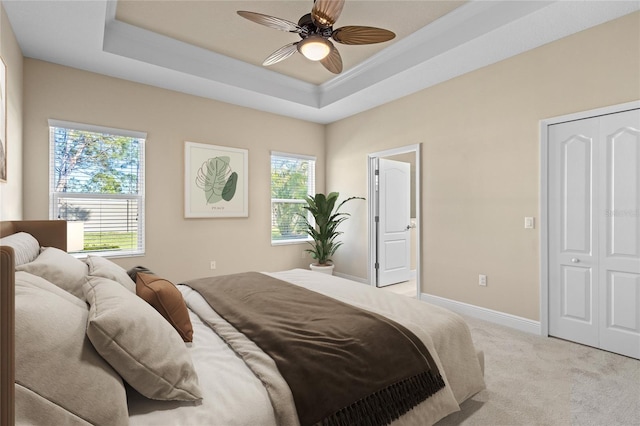 bedroom featuring a raised ceiling, crown molding, baseboards, light colored carpet, and ceiling fan