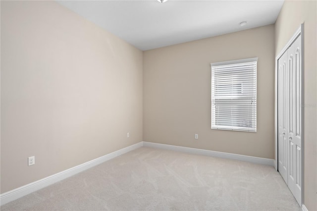 unfurnished bedroom with baseboards, a closet, and light carpet