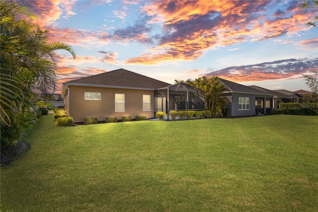 back of house with glass enclosure, a lawn, and stucco siding