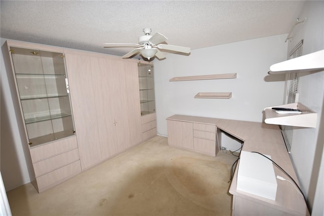 unfurnished office featuring light colored carpet, a textured ceiling, built in study area, and a ceiling fan