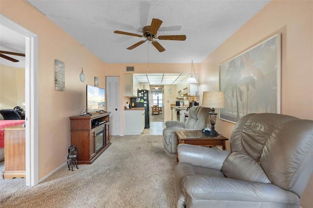 living area featuring visible vents, baseboards, ceiling fan, light colored carpet, and a textured ceiling