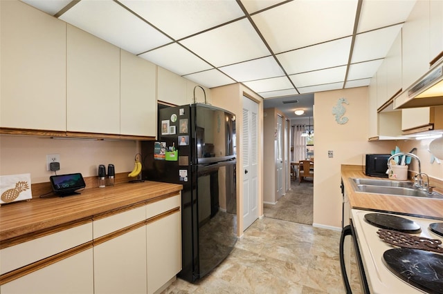 kitchen with a drop ceiling, cream cabinets, freestanding refrigerator, white range with electric stovetop, and a sink