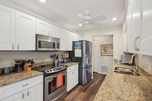 kitchen featuring dark wood-type flooring, a sink, appliances with stainless steel finishes, white cabinets, and decorative backsplash