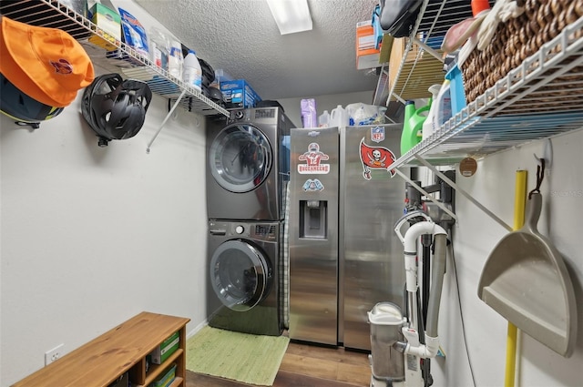 clothes washing area featuring laundry area, stacked washer / dryer, wood finished floors, and a textured ceiling