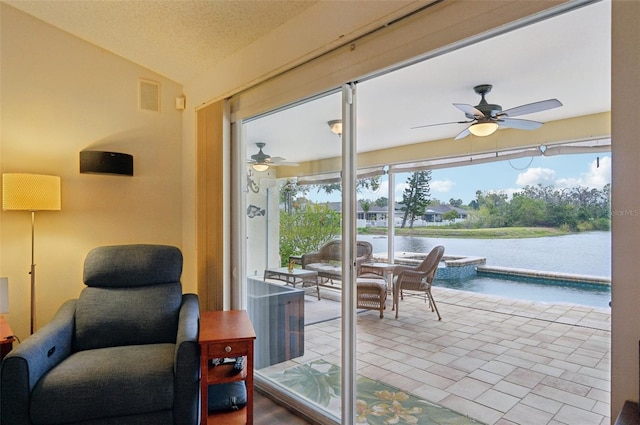 sitting room with visible vents, ceiling fan, vaulted ceiling, a water view, and a textured ceiling