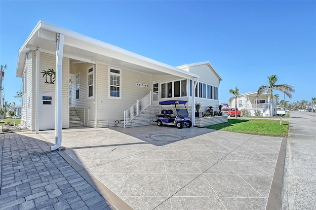 exterior space featuring a front lawn, an attached carport, driveway, and a sunroom