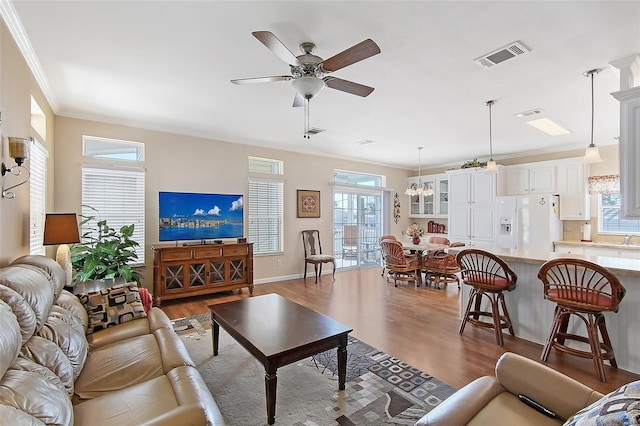 living area with visible vents, crown molding, baseboards, wood finished floors, and a ceiling fan