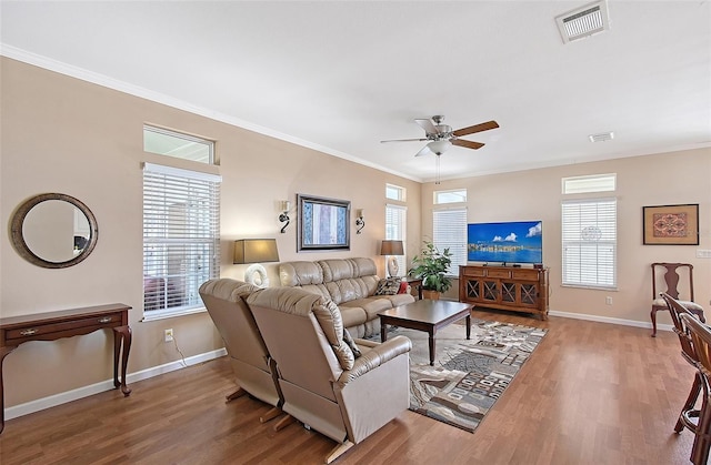 living area featuring a ceiling fan, wood finished floors, visible vents, baseboards, and crown molding