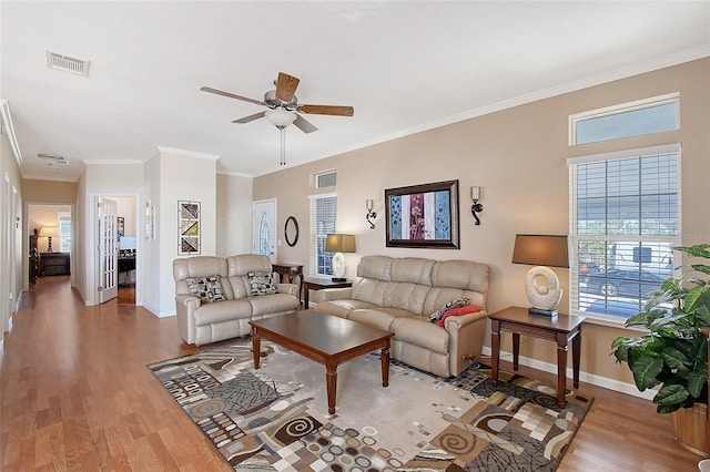 living area with ornamental molding, wood finished floors, visible vents, and baseboards