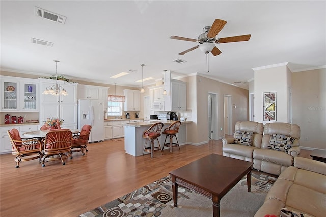 living room with light wood-type flooring, ceiling fan with notable chandelier, visible vents, and ornamental molding